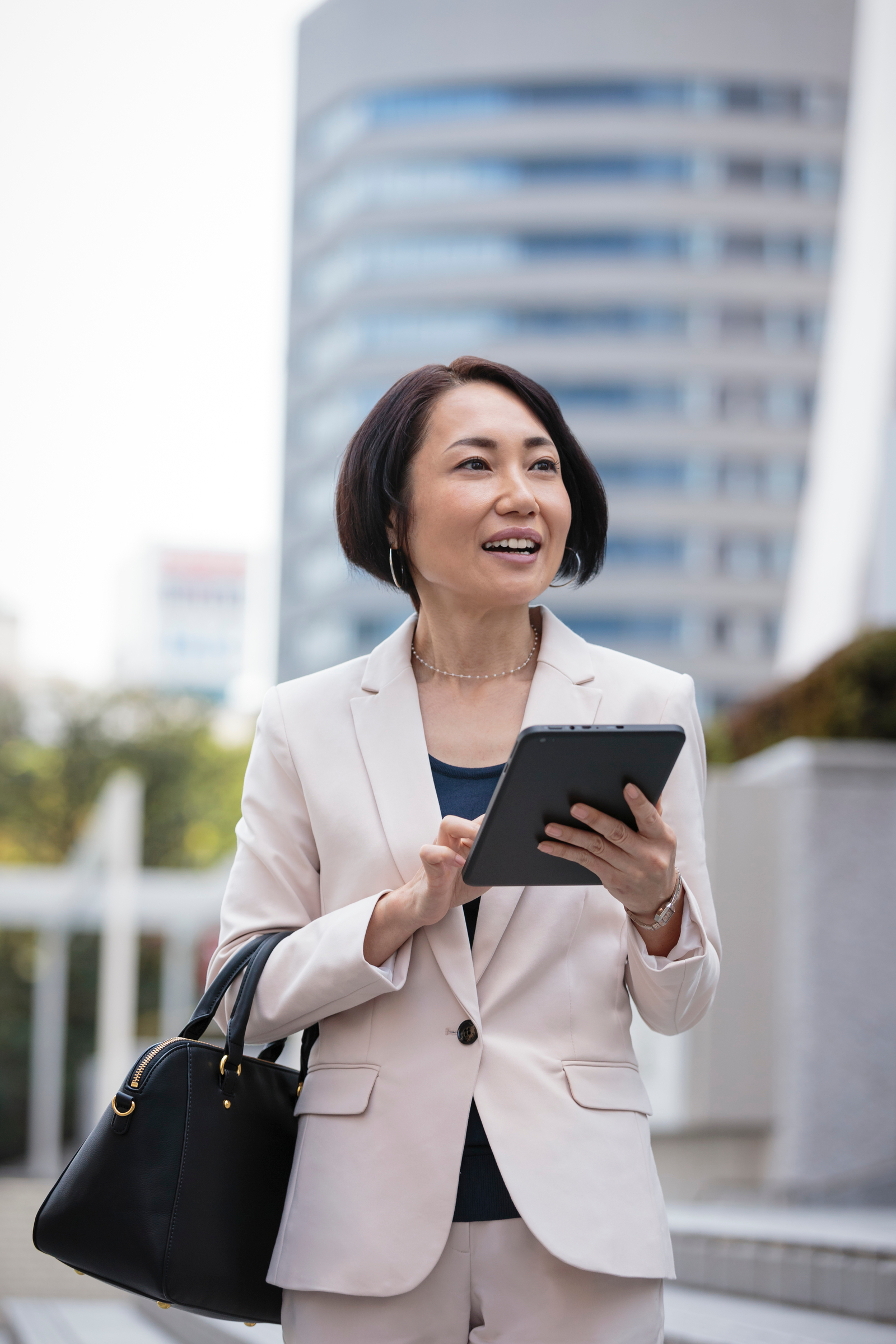 Close up of businesswoman using digital tablet and carrying briefcase walking under highrise buildings in cityscape